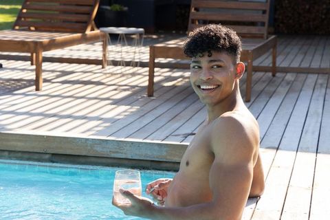 Smiling african american man lounging poolside holding tumbler on sunny backyard deck