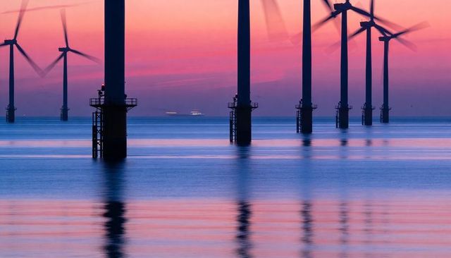 Offshore wind turbines at dusk reflecting on calm sea with pink and purple twilight