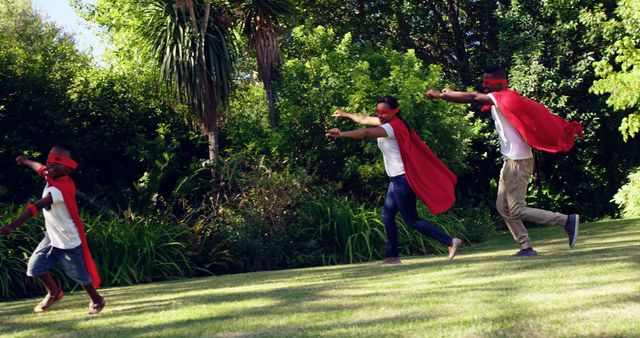 African American children and a young adult are playfully running outdoors dressed in superhero capes and masks, with copy space. Their energetic playtime captures a moment of joy and imagination in a lush green park setting.