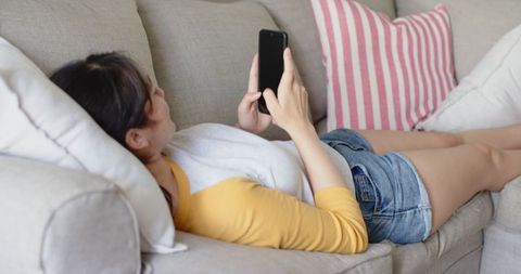 Asian Woman Relaxing on Sofa Engages with Smartphone