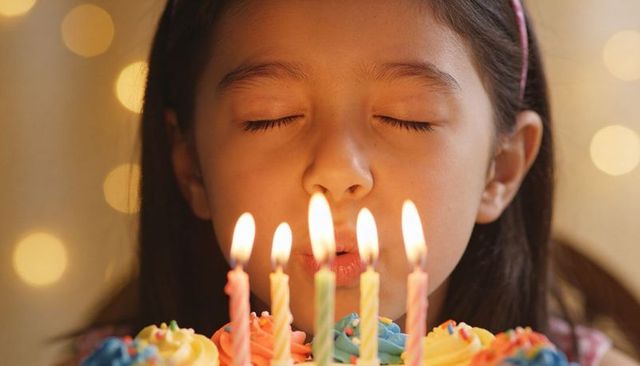 Young girl blowing birthday candles on colorful cupcake cake with bokeh lights