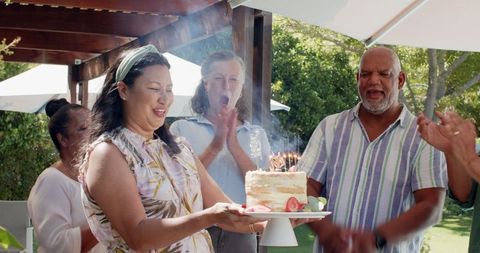 Joyful reunion with elderly friends celebrating with cake in sunny garden