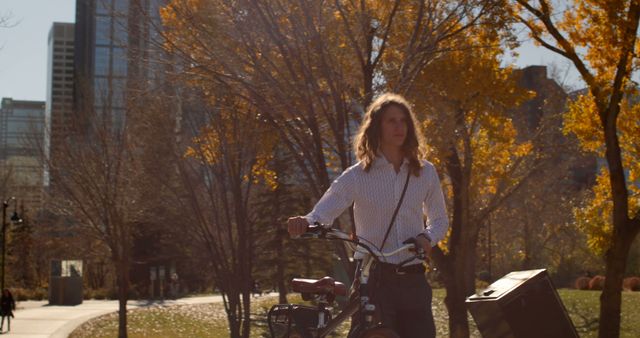 Person using bicycle as means of transport through an autumn park. Suitable for themes of urban lifestyle, relaxing, outdoor activities, and seasonal changes. The city skyline in background suggests a balance of nature and urban living.