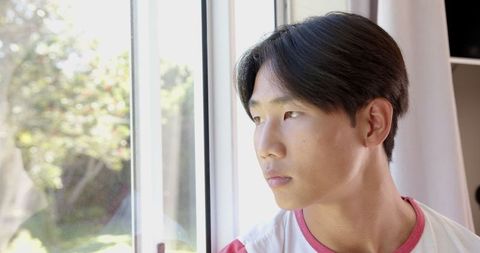 Pensive teen gazing out sunlit window into garden