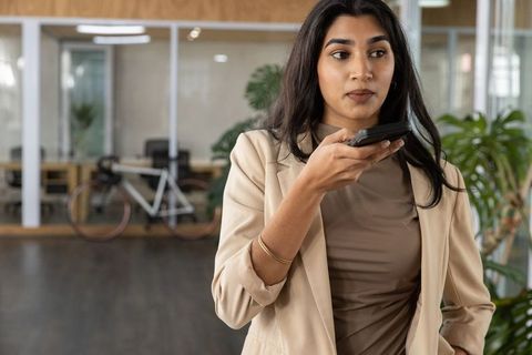 Indian businesswoman holding smartphone speaking in modern coworking office space with greenery