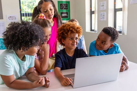 Diverse Elementary Students Collaborating on Laptop, Learning Together in Bright Classroom