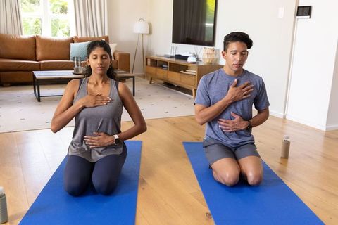 African american couple practicing mindful breathwork on blue mats in modern living room