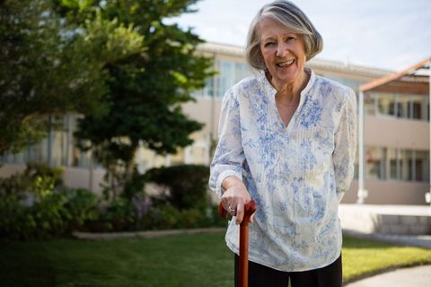 Senior woman smiling outdoors with walking cane in garden