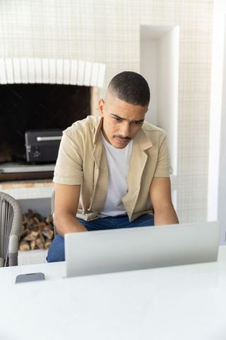 Focused man in his 30s working on laptop at home minimalist modern interior with fireplace