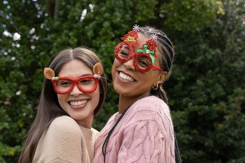 Smiling diverse young women wearing festive red glitter novelty glasses outdoors
