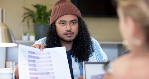 Multicultural coworker presenting purple bar chart, pointing at laptop during collaborative planning