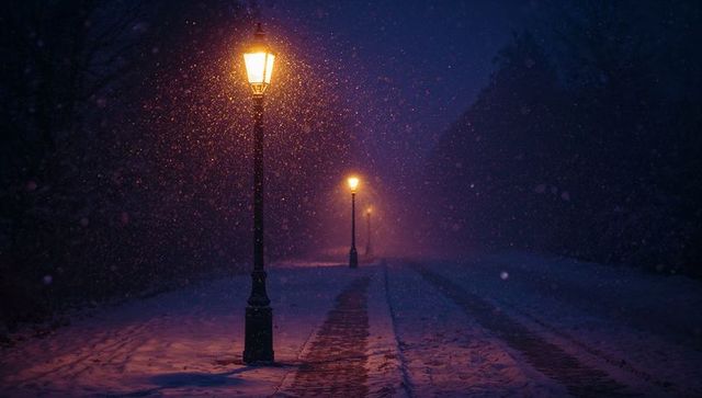 Ornate lampposts casting warm amber light on snowy walkway at night with falling snow and lantern gl