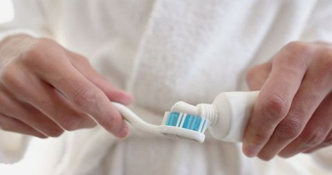 Person Applying Toothpaste onto Toothbrush in Bathroom
