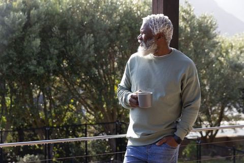 Senior african american man relaxing on balcony holding mug and enjoying morning sunlight