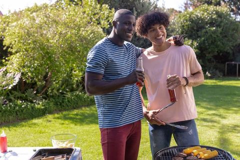 Smiling Black and Mixed-Race Friends Grilling Burgers and Corn at Sunny Backyard BBQ