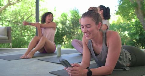 Diverse women practicing yoga on patio with mats, water bottles and fitness trackers