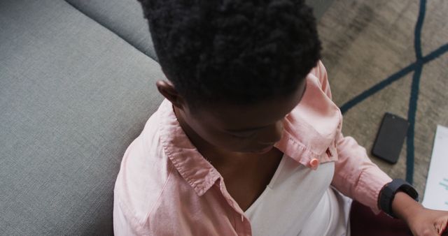 Person sitting on the floor next to a couch using a smartphone seen from above. Ideal for concepts of remote work, relaxation, home lifestyle, and technology use.