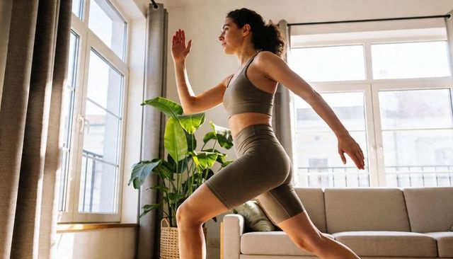 Woman lunging in olive activewear performing dynamic home workout in sunlit living room
