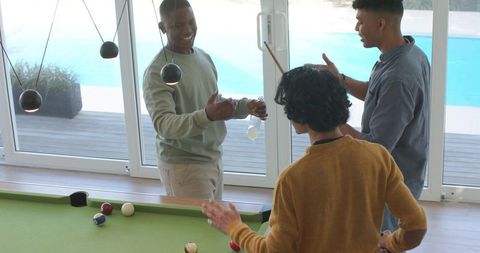 Young diverse friends playing casual indoor billiards and socializing by pool deck