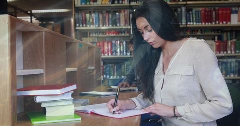 Young woman studying and writing at library carrel with textbooks and spiral notebook