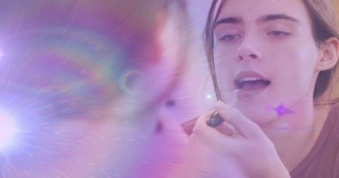 Young woman applying lip balm at mirror with dreamy lens flare and pastel bokeh
