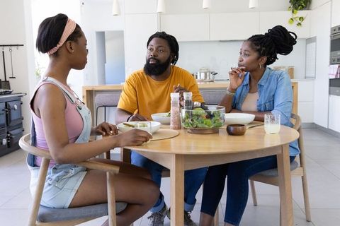 African american family sharing healthy dinner at modern kitchen round table, talking