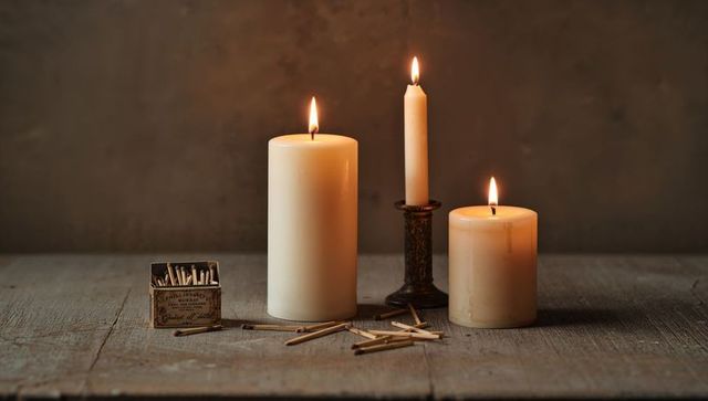 Glowing trio of candles casting warm amber light on rustic wooden table with matchbox