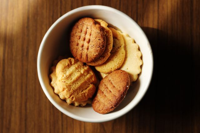 Close-up of an assortment of biscuits in a white bowl placed on a wooden table. Ideal for use in food blogs, recipe websites, dessert menus, and advertisements for bakeries or snack products.