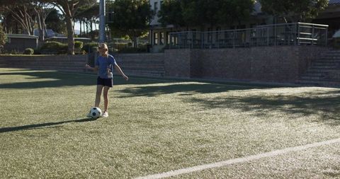Preteen girl practicing soccer dribbling on sunlit school turf with ample copy space