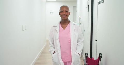 Smiling african american nurse standing in bright clinic corridor wearing pink scrubs