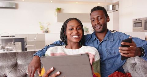 Happy African American Couple Relaxing with Tablet and Smartphone in Living Room