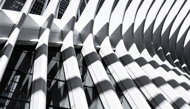 Curved architectural ribs casting diagonal shadows across modern urban glass facade