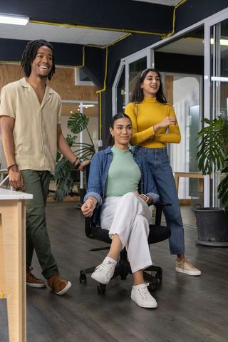 Diverse team collaborating in open-plan office around seated colleague in rolling chair