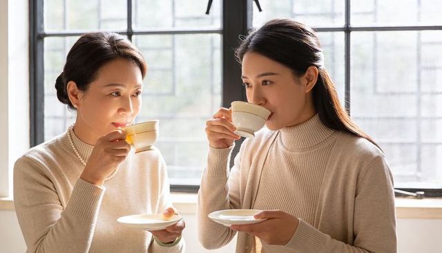 Mother and daughter sharing afternoon tea by sunlit window, sipping porcelain cups