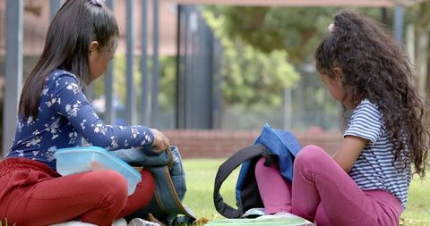 Two Girls Relaxing in Schoolyard Unpacking Backpacks