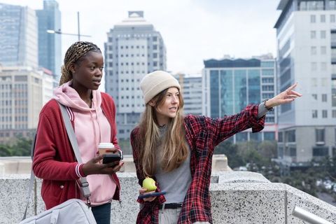 Black and white friends pointing on urban rooftop holding coffee and apple in plaid layers