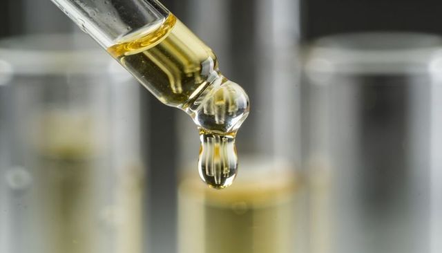 Glass pipette releasing amber droplet over test tubes macro laboratory close-up precision