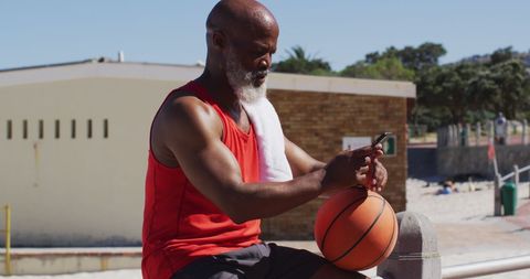 Senior man with basketball and smartphone by beach
