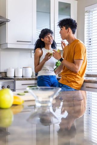Multiracial couple enjoying green smoothies while chatting on modern kitchen countertop