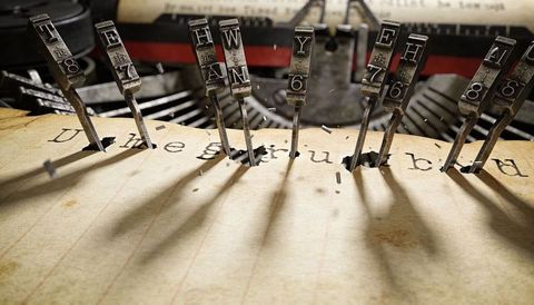 Typebars striking aged lined paper, creating deep indentations and flying ink flecks