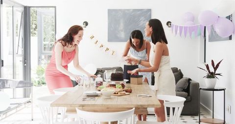 Three women setting table for birthday celebration in bright dining room
