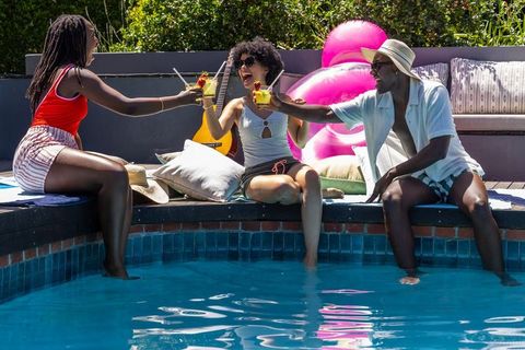 African american friends toasting by pool with cocktails and flamingo float
