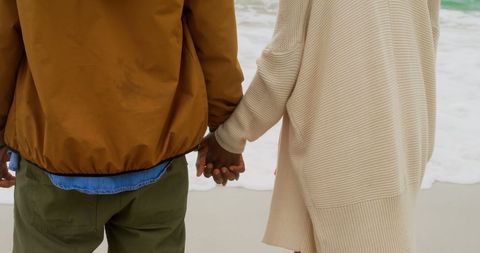 Romantic Couple Holding Hands on Beach in Cozy Clothing