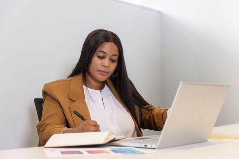 African american professional woman in blazer writing notes while checking laptop swatches