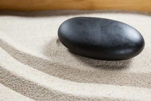 Smooth black pebble resting on white sand creating a tranquil and balanced scene. Ideal for use in spa and wellness designs, meditation materials, zen garden concepts, and nature-related themes. Captures the essence of simplicity and harmony.