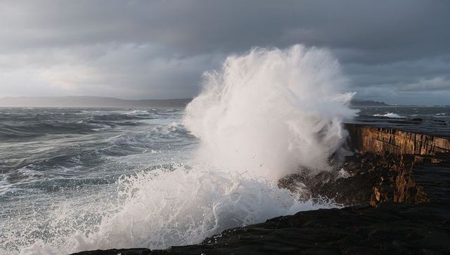 Giant wave crashing against rugged seawall sending towering white spray on stormy coast