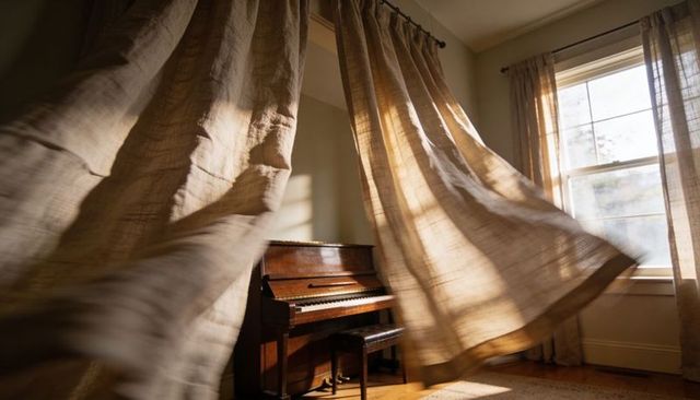 Sunlit upright piano with billowing linen curtains in serene minimalist interior