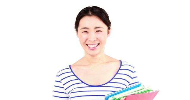 Young woman smiling while holding notebooks against a white background. Useful for educational materials, school promotions, back-to-school campaigns, and articles about student life and learning.