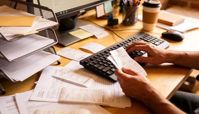 Hands sorting receipts over keyboard amid cluttered desk for small business accounting