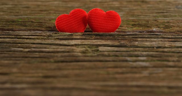 Red fabric hearts placed side by side on a weathered wooden surface conveying love and affection. Great for Valentine's Day, romantic greetings, cards, or anniversary themes. The rustic charm contrasts the bright hearts, emphasizing romantic and heartfelt moments.